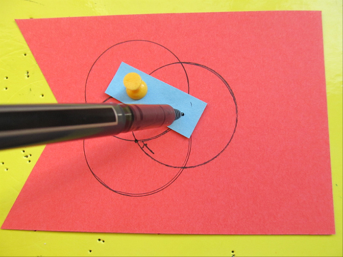 Put the pin in one of the holes on the strip and through the hole you just made on the paper.
Put the pen point in the second hole and rotate it to draw another circle.
