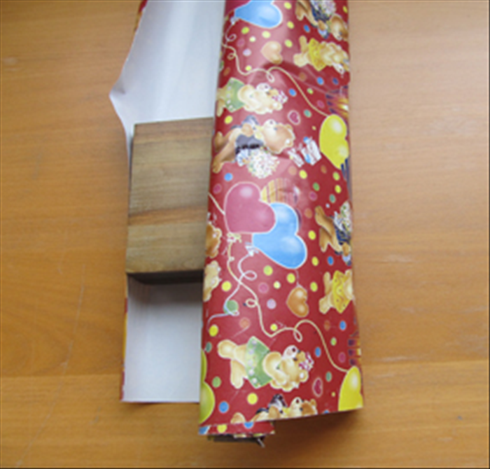 Bring the rolled paper over the top of the present.
Make a crease mark where the paper touches the top of the side.
