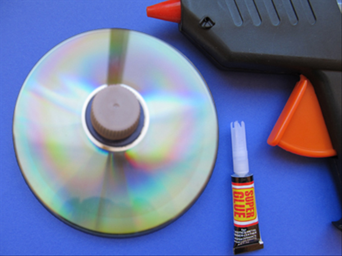 Place the cd on the table with the shiny side facing up.
Glue the plastic bottle cap to the center.
