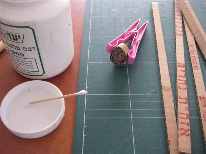 Coat one side of a strip with glue and roll it up tightly. Hold it together with the clothespin until the glue is dry.

Do this for 10 strips of coardboard
