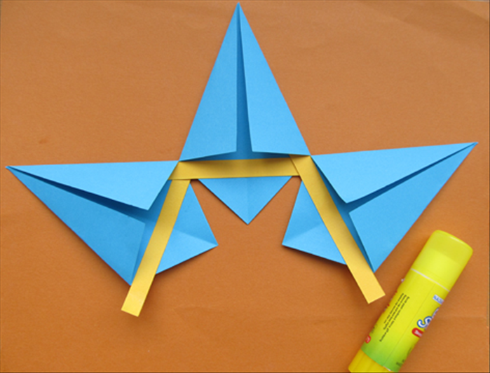 Place another kite on the right.
Put glue on the left edge of its strip. Stick the strip into the flap of the middle kite.

Make sure the edge of the kite is horizontal with the flaps of the center kite shape.

