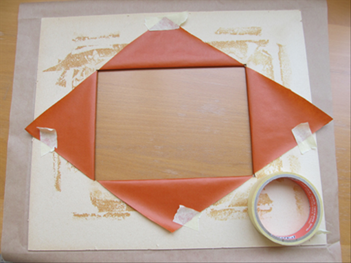 Place the paper or material facedown. 
Place the mat on top of it.
Make sure the ends of the cuts match up to the corners of the window of the mat.

Pull the triangle tops snugly up and over the window of the mat and tape them in place.

Turn the mat over to check if there are no wrinkles and it is aligned.
Adjust if needed

