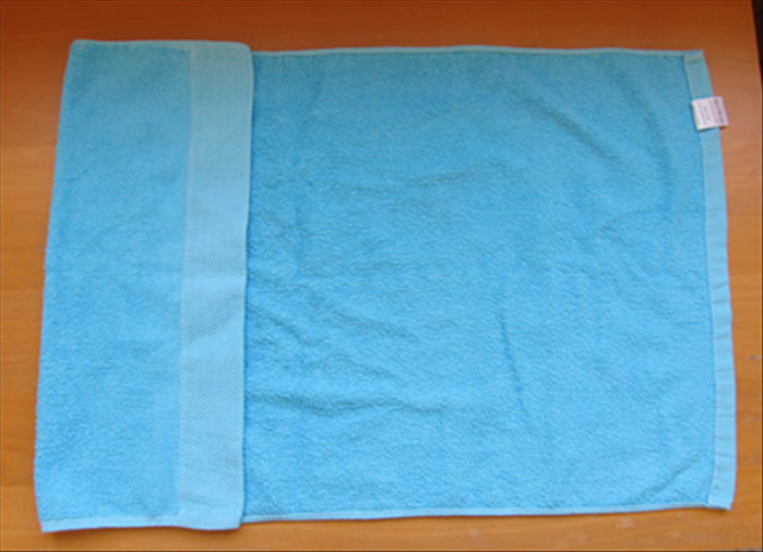 Open up the towel with the short edges at the sides.

 Fold  the left  edge about  ¼ of the way to the right edge.

