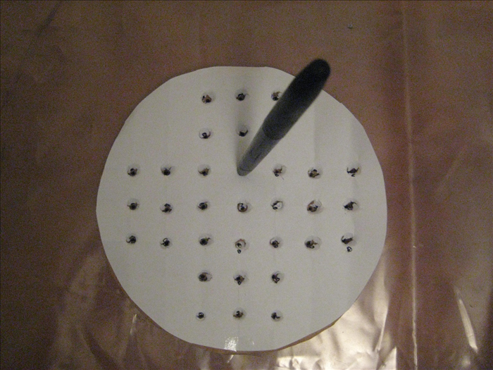 Use an old pen to punch holes through the dots.
Wiggle it around to enlarge the holes

Put a marble on the holes to see it it stay put. If not Wiggle the pen in the holes to enlarge them.