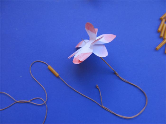 Measure the length of string you need around your neck and add enough to easily knot it.
Thread the string on a needle.

Pull one straw piece through the needle and then the flower by pushing the the needle through the center of the flower.
