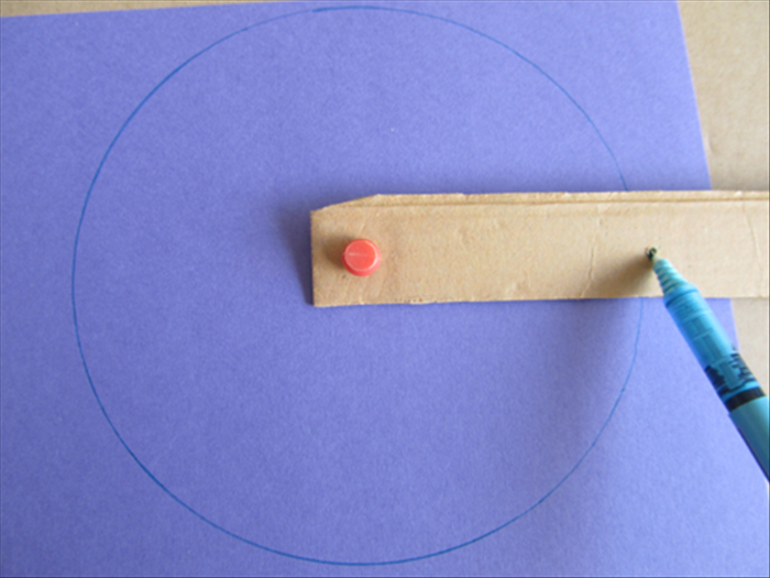 <p> Place the blue paper on top of cardboard.</p> 
<p> Insert the push pin through the hole at the end of the strip and the center of the paper.</p> 
<p> Put the pen point in the other hole and rotate it to draw a circle.</p> 
<p> Cut out the circle</p> 
<p>  </p>