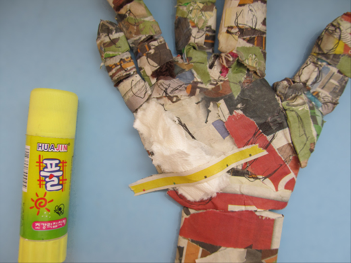 Put glue on one side of newspaper strips. Place them on top of the toilet paper and around the sides.