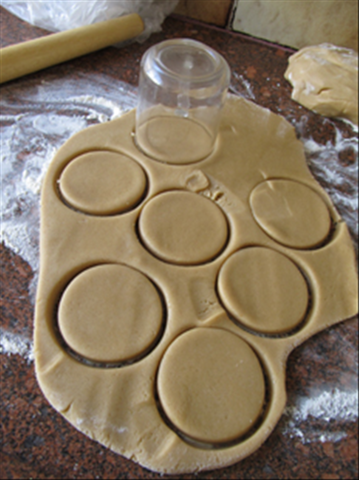 Press the cup into the dough to cut circles. 
Leave them in place and pull up the dough outside of the circle. Gather it to roll out again for more cookies.
