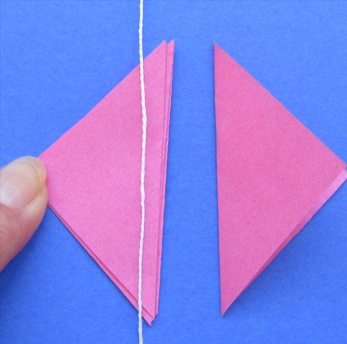 You should have 3 triangles glued and one left over

Place the string near the long edge of the 3 glued triangles
Put glue on the 4th triangle and align it on top
