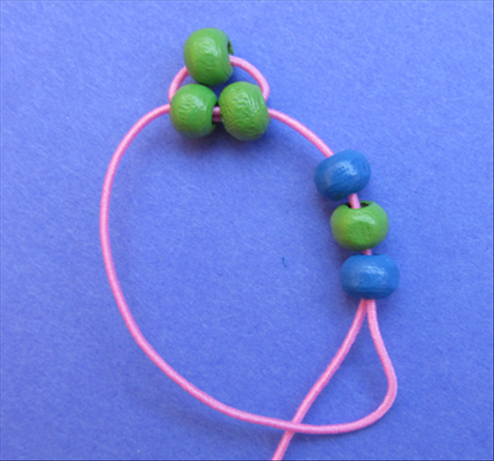 Bring the end of the left string around, into and through the right side of the 3 beads.
Pull the end until the beads straighten out under the 2 beads on top. 
See the next picture for result.
