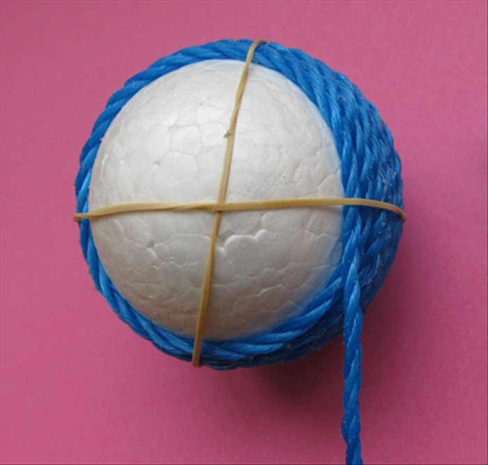 Glue and wind the cord around the ball. Hold in place with the rubber bands while the glue dries.
