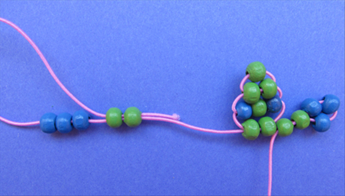 Insert 2 green beads then 3 blue beads on the left side. 
Insert the end of the left string into and through the 2 green beads from the left side.  
Pull the end of the string to tighten and move the beads up against the right side of the lizard.